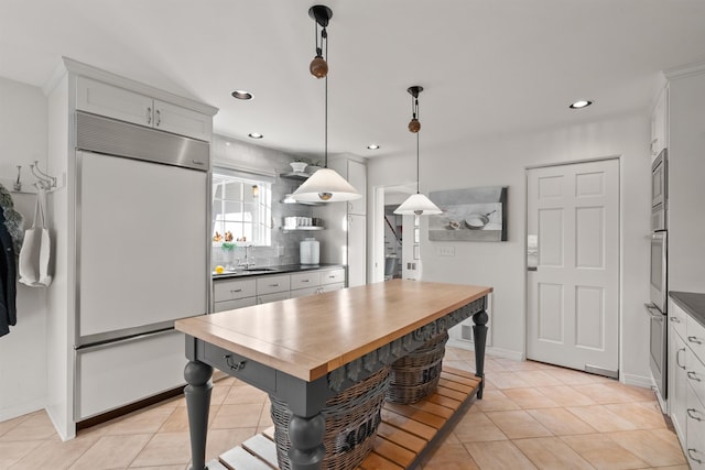 kitchen featuring butcher block countertops, open shelves, decorative light fixtures, tasteful backsplash, and built in appliances