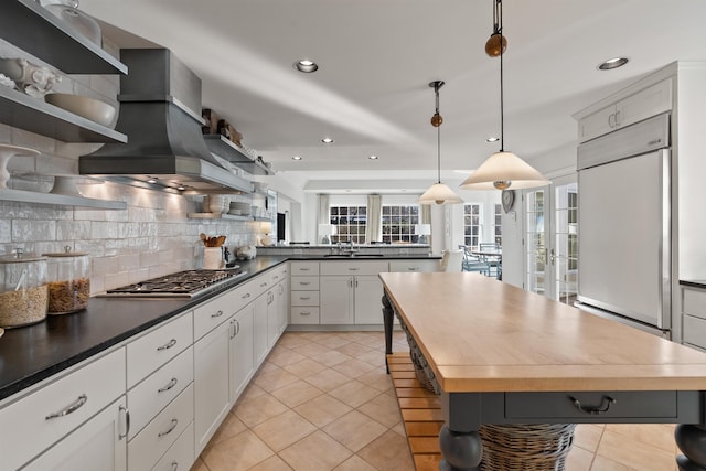 kitchen featuring stainless steel gas cooktop, built in refrigerator, light tile patterned floors, decorative backsplash, and open shelves