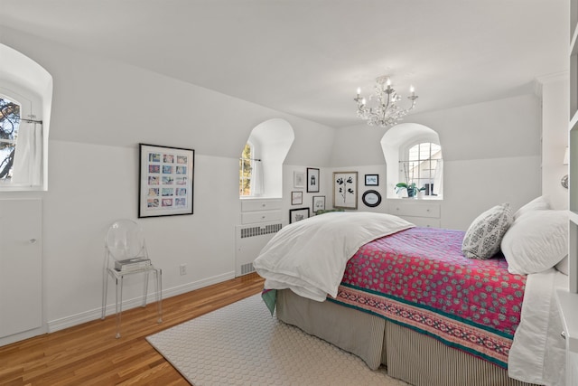 bedroom featuring lofted ceiling, wood finished floors, radiator, an inviting chandelier, and baseboards