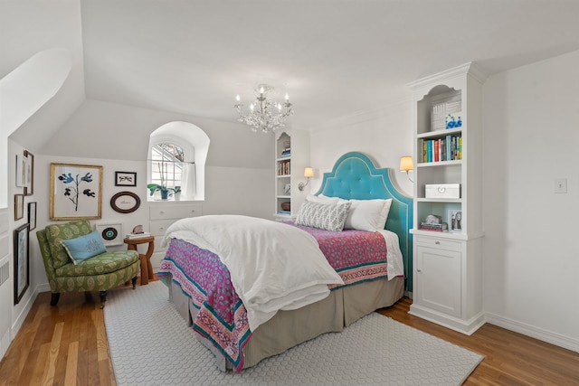 bedroom featuring baseboards, lofted ceiling, an inviting chandelier, and wood finished floors