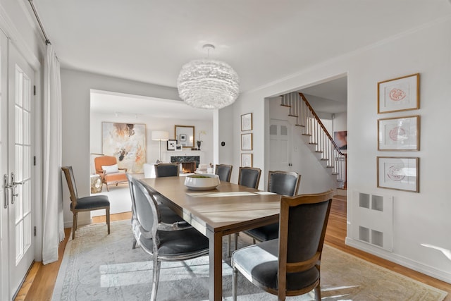 dining room with visible vents, light wood-style flooring, a warm lit fireplace, and stairs