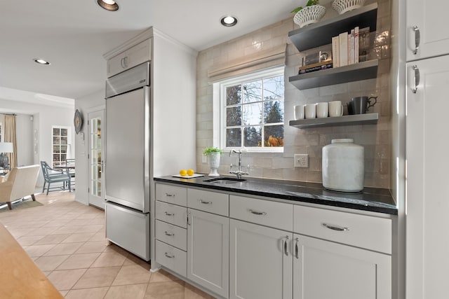 kitchen with light tile patterned floors, open shelves, a sink, decorative backsplash, and built in refrigerator