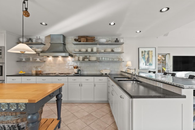 kitchen with open shelves, custom range hood, a peninsula, stainless steel appliances, and a sink