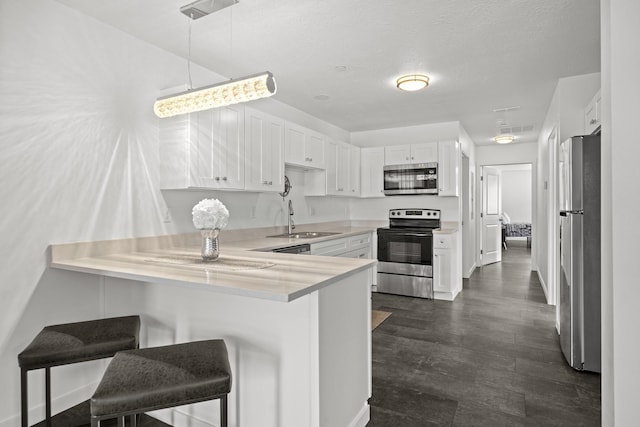 kitchen featuring a peninsula, stainless steel appliances, light countertops, white cabinets, and a kitchen bar