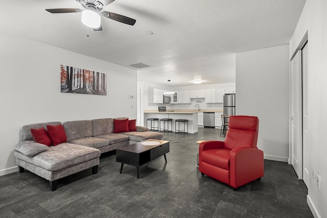 living area with visible vents, baseboards, a textured ceiling, and ceiling fan