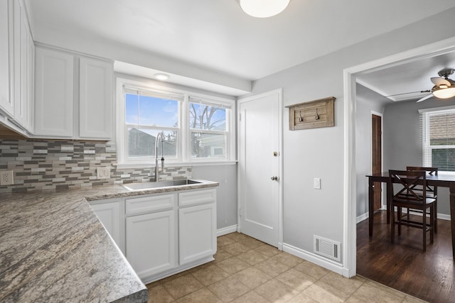 kitchen with baseboards, visible vents, a sink, decorative backsplash, and white cabinets