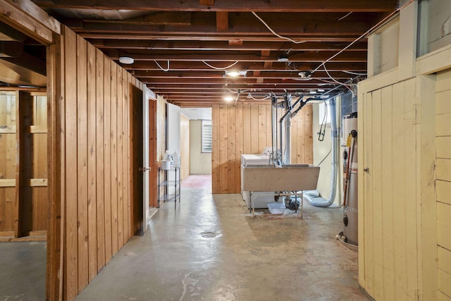 unfinished basement featuring a sink, wooden walls, and water heater