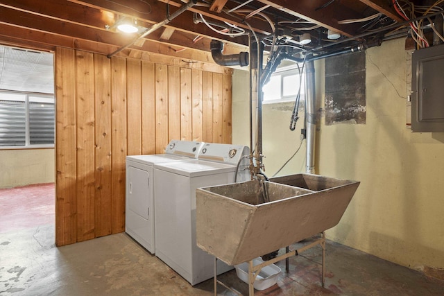 laundry room featuring wood walls, electric panel, laundry area, washer and dryer, and a sink