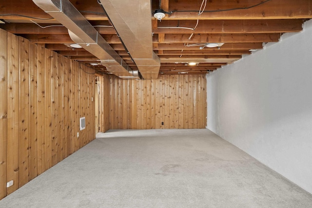 unfinished below grade area featuring wooden walls, carpet, and visible vents