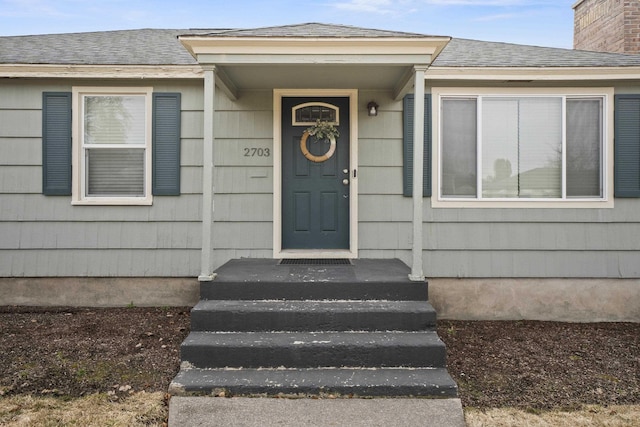 view of exterior entry with roof with shingles