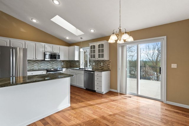 kitchen with vaulted ceiling with skylight, white cabinets, stainless steel appliances, and glass insert cabinets