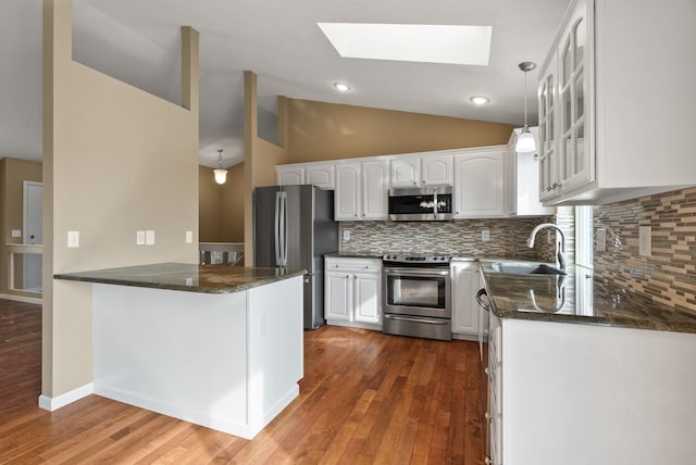 kitchen featuring a sink, dark stone countertops, appliances with stainless steel finishes, a peninsula, and glass insert cabinets