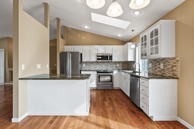 kitchen featuring glass insert cabinets, vaulted ceiling with skylight, appliances with stainless steel finishes, and white cabinetry