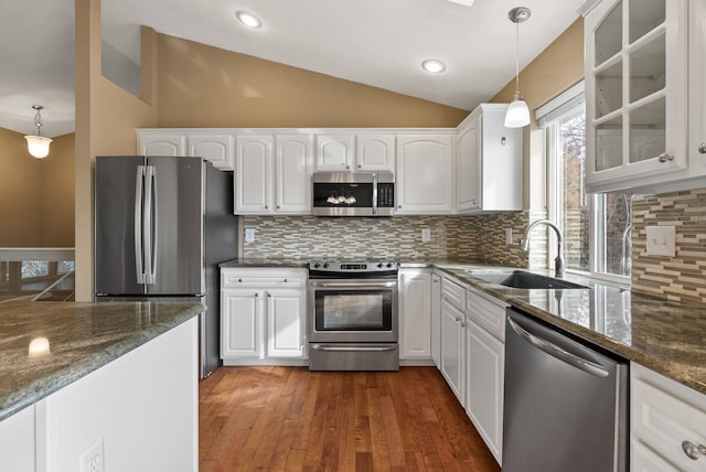 kitchen with a sink, white cabinetry, appliances with stainless steel finishes, glass insert cabinets, and vaulted ceiling