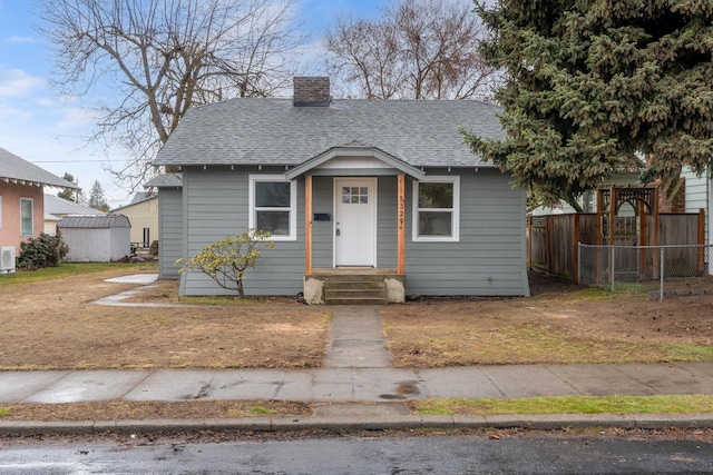 bungalow-style home featuring a chimney, roof with shingles, and fence