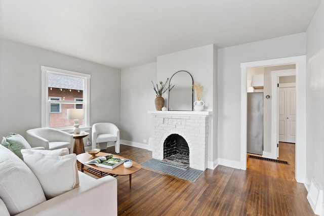 living room with visible vents, a brick fireplace, wood finished floors, and baseboards