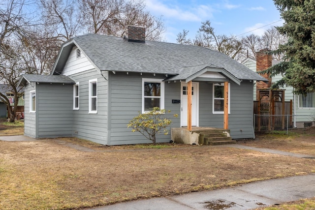 bungalow featuring a chimney, a shingled roof, and fence