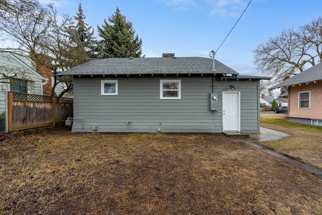 back of property with fence and a shingled roof