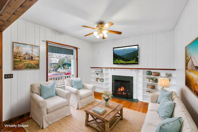 living room with a ceiling fan, wood finished floors, and a warm lit fireplace