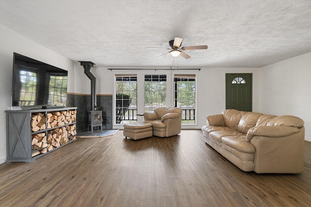 living area with wood finished floors, a textured ceiling, ceiling fan, and a wood stove