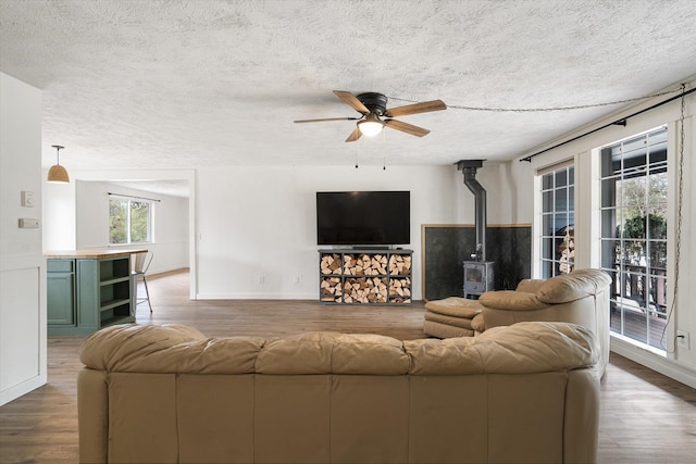 living area with a textured ceiling, a wood stove, a ceiling fan, and wood finished floors