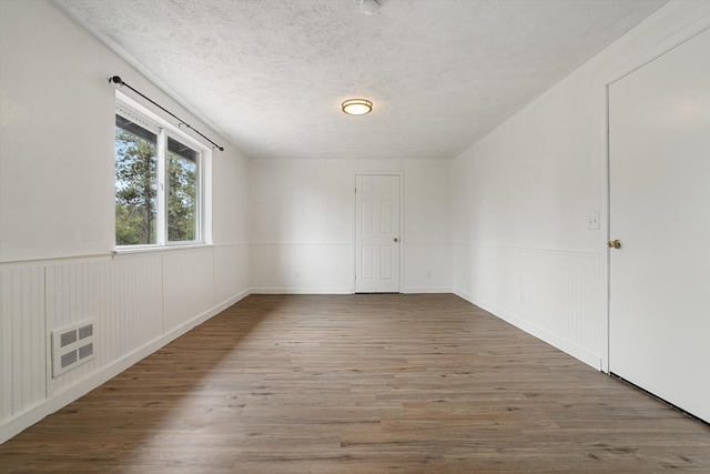 spare room featuring wainscoting, wood finished floors, visible vents, and a textured ceiling