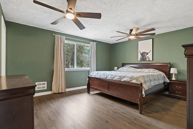 bedroom featuring visible vents, ceiling fan, baseboards, wood finished floors, and a textured ceiling