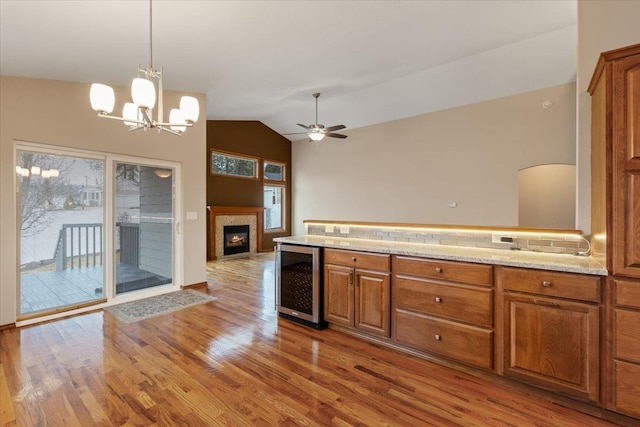 kitchen with beverage cooler, vaulted ceiling, brown cabinets, wood finished floors, and a glass covered fireplace