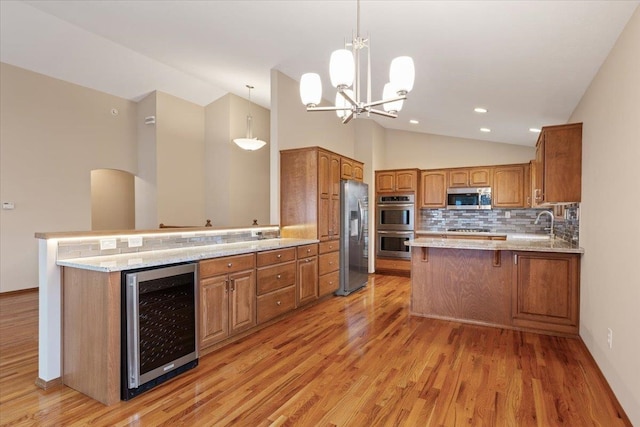 kitchen with beverage cooler, stainless steel appliances, a peninsula, brown cabinetry, and vaulted ceiling