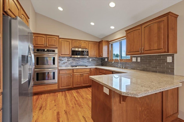 kitchen with a sink, brown cabinets, appliances with stainless steel finishes, and a peninsula