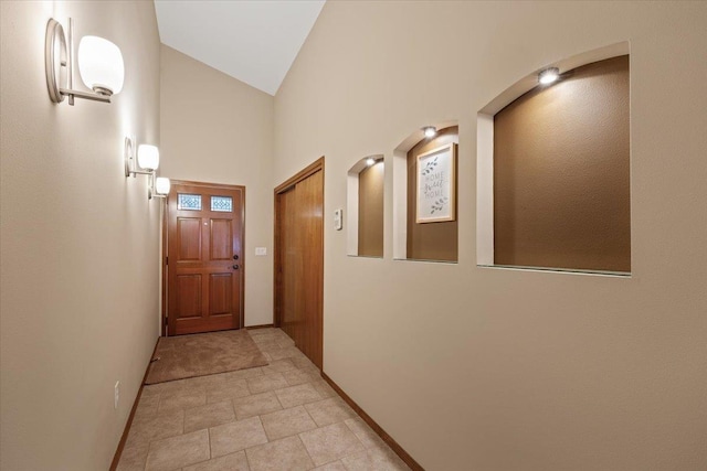 corridor featuring baseboards and high vaulted ceiling