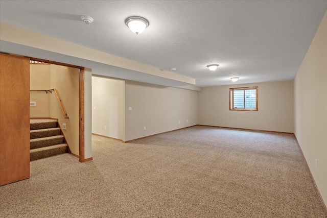 basement featuring stairway, baseboards, carpet floors, and a textured ceiling