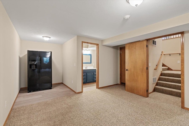 interior space with stairway, baseboards, a sink, light colored carpet, and black refrigerator with ice dispenser