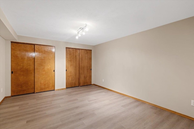 unfurnished bedroom with baseboards, light wood-type flooring, and two closets