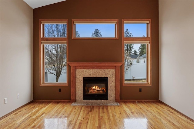 unfurnished living room with plenty of natural light, a warm lit fireplace, and wood finished floors