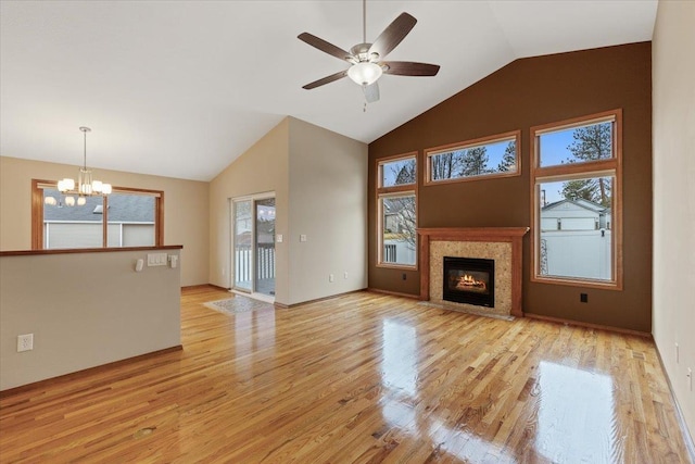 unfurnished living room with a fireplace with flush hearth, ceiling fan with notable chandelier, light wood finished floors, and high vaulted ceiling