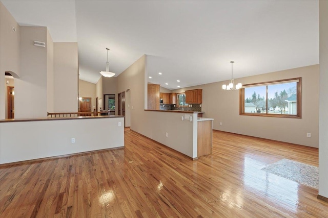 kitchen with light wood finished floors, lofted ceiling, a peninsula, brown cabinets, and a chandelier