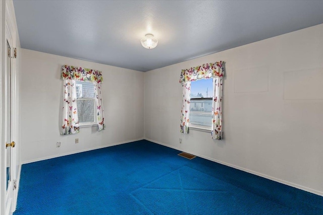 empty room featuring a wealth of natural light, visible vents, baseboards, and carpet flooring