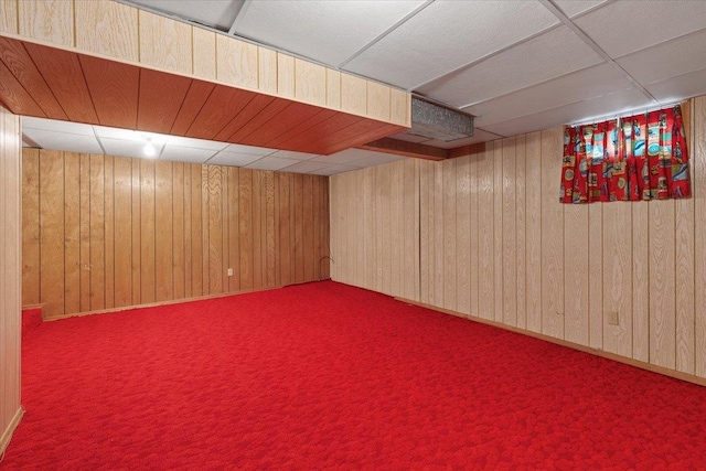 finished below grade area with carpet flooring, a paneled ceiling, and wooden walls