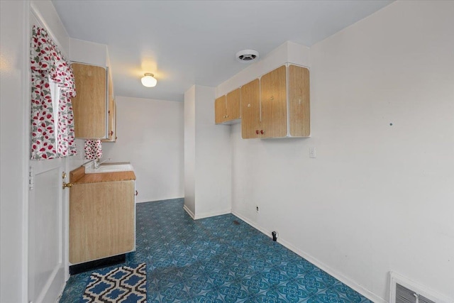 kitchen featuring visible vents, baseboards, dark floors, light countertops, and a sink