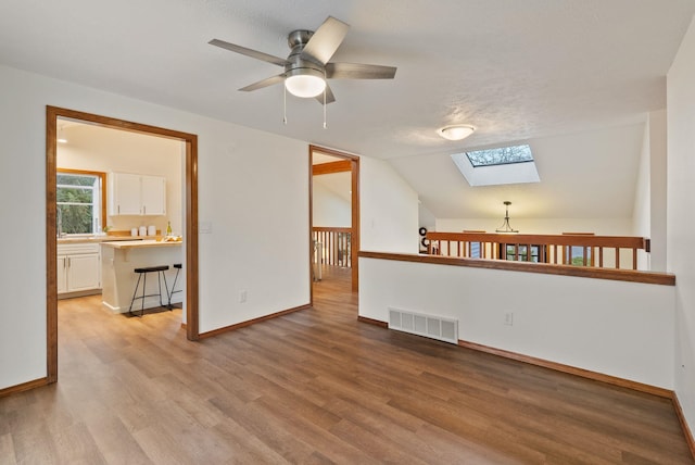 unfurnished living room featuring visible vents, baseboards, vaulted ceiling with skylight, light wood-style floors, and a ceiling fan