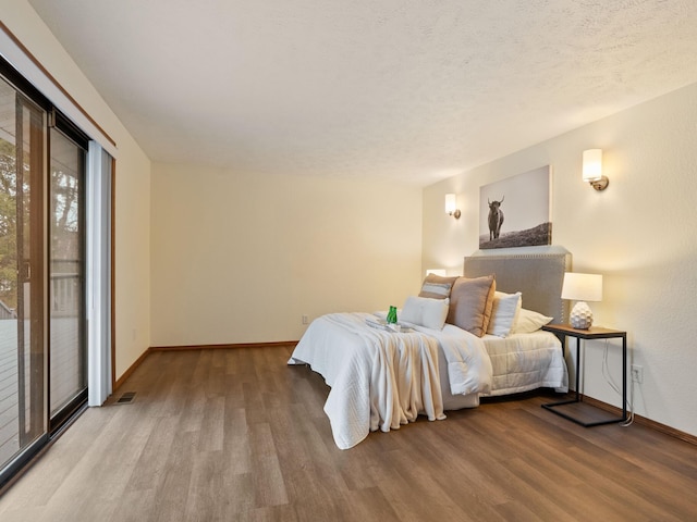 bedroom featuring visible vents, baseboards, a textured ceiling, and wood finished floors