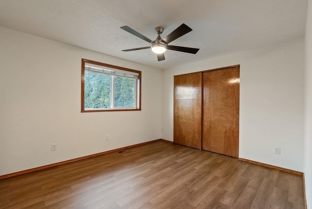 unfurnished bedroom featuring wood finished floors, baseboards, a closet, and ceiling fan