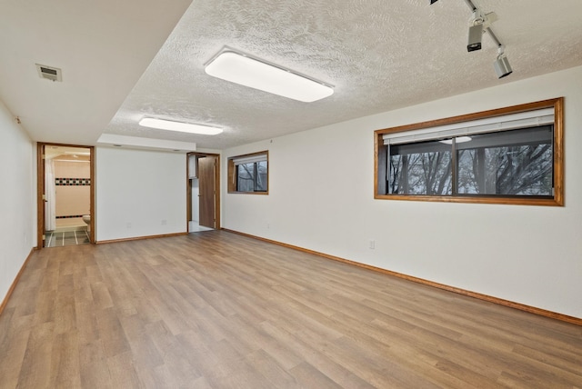 unfurnished room with light wood finished floors, visible vents, a textured ceiling, and baseboards