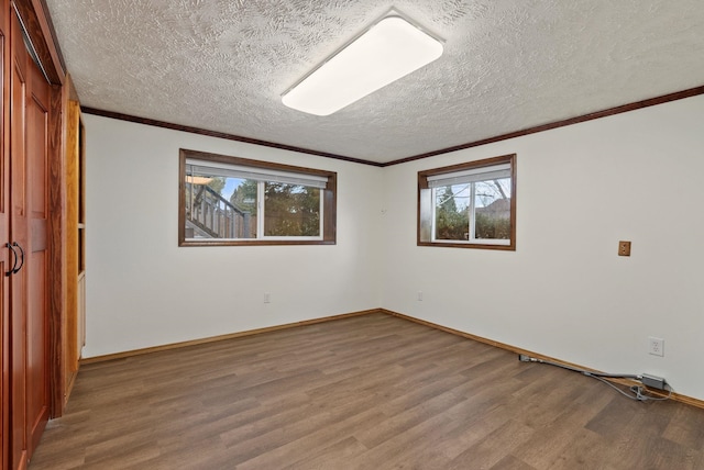 unfurnished room featuring baseboards, a textured ceiling, wood finished floors, and crown molding