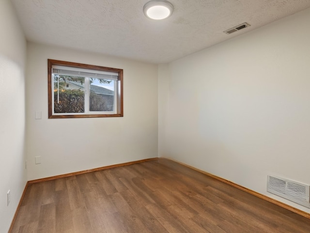 empty room featuring visible vents, a textured ceiling, and wood finished floors