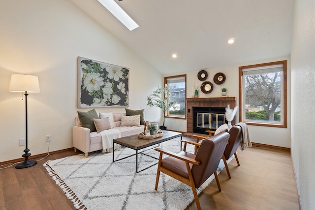 living area with plenty of natural light, a brick fireplace, a skylight, and wood finished floors