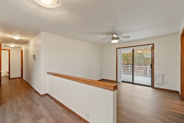 corridor with wood finished floors, baseboards, and a textured ceiling