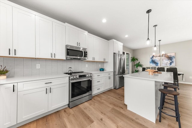 kitchen featuring light wood-type flooring, a kitchen bar, light countertops, decorative backsplash, and stainless steel appliances