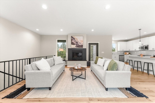 living room featuring recessed lighting, a glass covered fireplace, and light wood finished floors